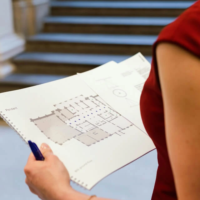 Close-up of a designer in a red dress reviewing detailed blueprints in a brightly lit interior.