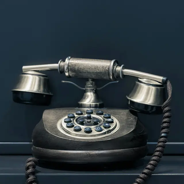 An antique-style telephone with a wooden base and silver metal handset against a dark blue background. (Image copyright: Pawel Czerwinski via Unsplash)