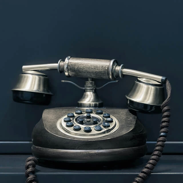 An antique-style telephone with a wooden base and silver metal handset against a dark blue background.