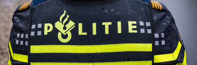 Close-up of a rain-wet Dutch police (Politie) vest, showing the force’s torch-and-shield logo and yellow reflective stripe across the back.