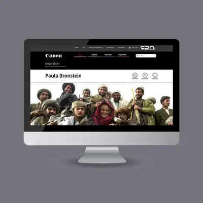 A desktop computer monitor showing a webpage under the “Inspiration” section of the Canon Professional Network site. The main focus of the screen is a wide banner image featuring a group of smiling people gathered together outdoors.
