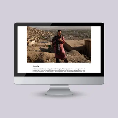 A desktop monitor displaying a website biography page. The upper half of the screen features a large, horizontal photograph of a woman wearing a patterned headscarf standing on a rocky hillside that overlooks a dense, widespread city below.