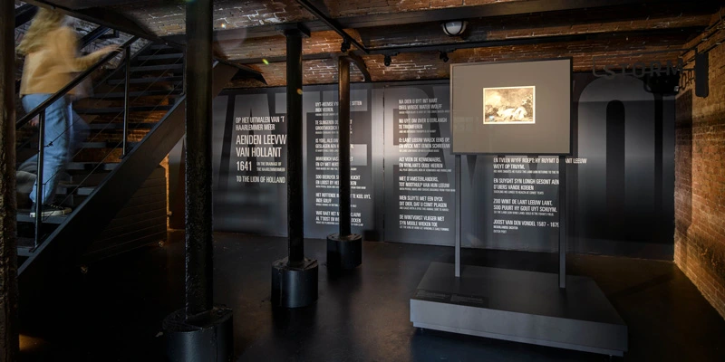 Woman ascending a staircase inside the museum, with typographic quotes from 17th-century poetry and documents displayed on the surrounding walls.