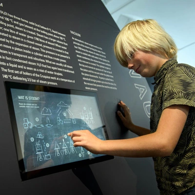 Young boy using a touchscreen embedded in a wall panel to learn about the properties and transformations of steam.