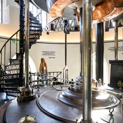 Visitor standing near the massive Cruquius engine installation, surrounded by large iron components and a spiral staircase inside the museum.