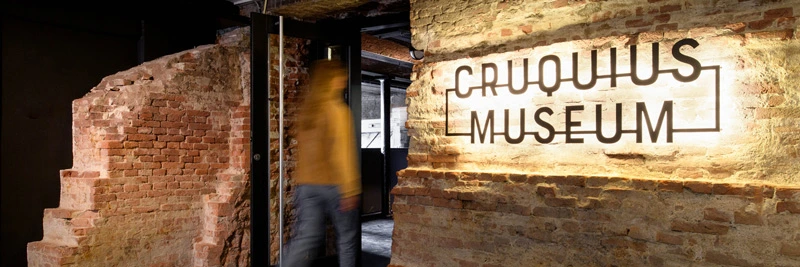 Entrance to the Cruquius Museum featuring exposed brick walls and illuminated signage, with a blurred figure walking through the doorway.