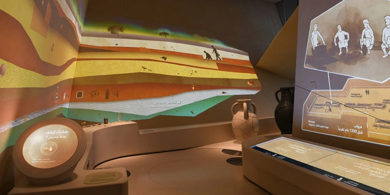 Wide view of the archaeological gallery, with large amphora replicas, touchscreen tables, and animated projections illustrating layers of earth and excavation scenes.