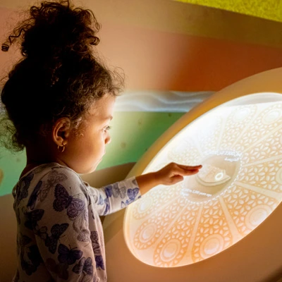 Close-up of a girl using a circular interactive screen that mimics ancient decorative patterns, part of an archaeology-themed activity about reconstructing cultural objects from fragments.