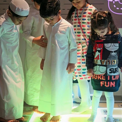 Group of children standing barefoot on a glowing interactive floor, focusing on triggering visual responses through movement.