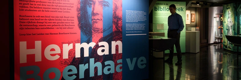 Entrance area of the exhibition featuring a large wall graphic with the name “Herman Boerhaave” and a silhouette cutout, with a man standing in a dimly lit space beyond the entrance.