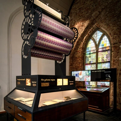 Banknote station with large printing rollers suspended above a display case of financial documents, set against an exposed brick wall and vibrant stained glass inspired by currency design.