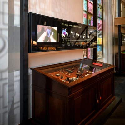 Display case containing metal printing tools and lead type molds, beneath a mounted infographic panel explaining the process of making lead type.
