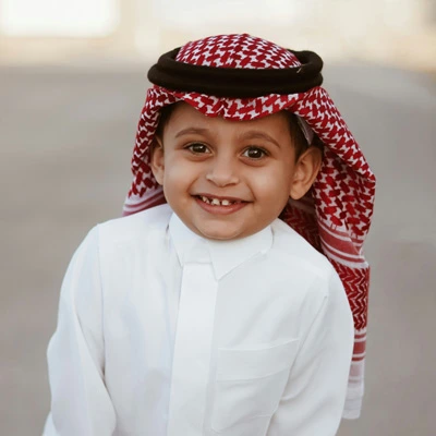 Portrait of a young boy smiling in traditional Saudi attire, representing the target audience of the educational initiative.