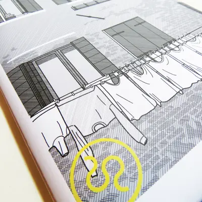 An internal page of a magazine featuring a grayscale architectural drawing of clotheslines hanging outside a building structure. A bright yellow circular graphic symbol is overlaid near the bottom of the page.