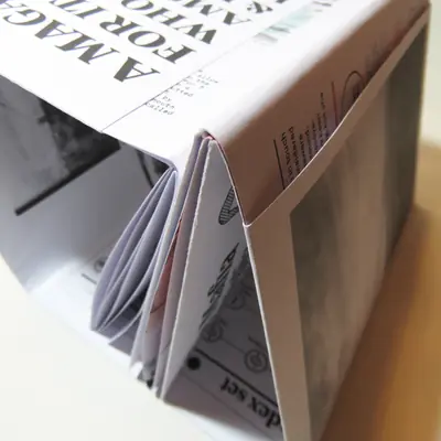 A close-up shot looking down into the complex zine-style folding structure of an open magazine. The unique layout reveals glimpses of inner pages with text, illustrations, and a distinct concertina fold.