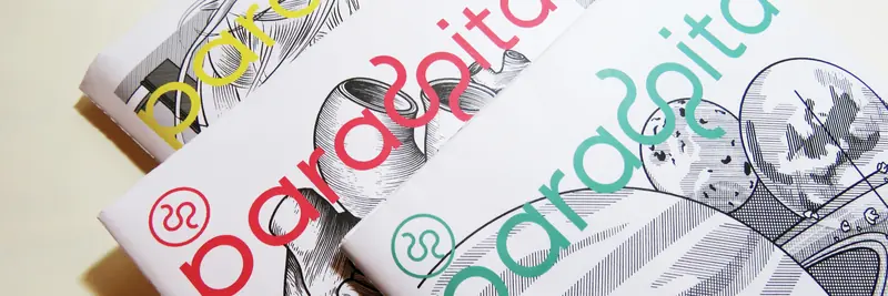 A cropped shot of three copies of “Parasita” magazine, stacked slightly overlapping. The title text is identical on all three, but colored differently in yellow, pink, and teal, over different black and white cover drawings.