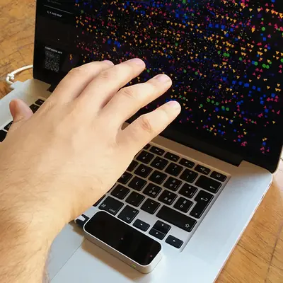 A person’s hand resting on top of a Leap Motion device near a MacBook trackpad while the screen shows the colourful extinction data visualisation with geometric shapes representing animal species.